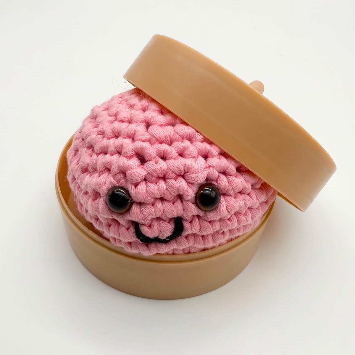 Crocheted smiling dumpling sitting in a miniature steamer basket