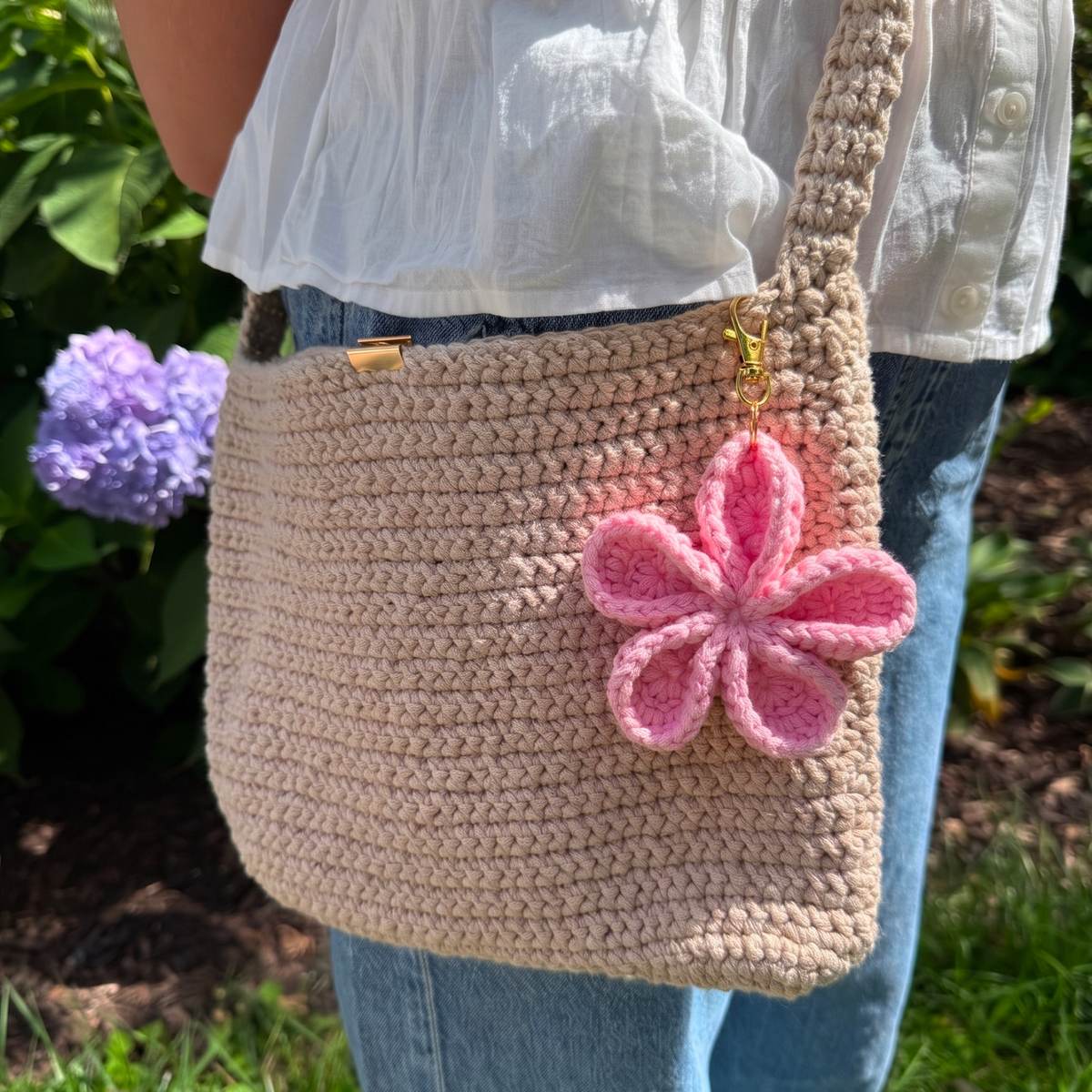 The flower charm clipped to a tan crochet crossbody bag